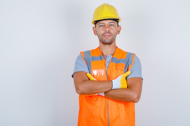 Constructor masculino en uniforme de pie con los brazos cruzados y mirando confiado, vista frontal.