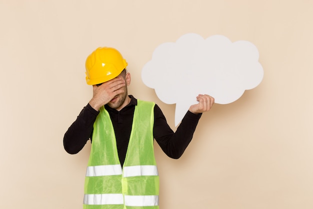 Constructor masculino de vista frontal en casco amarillo con gran cartel blanco sobre el fondo claro