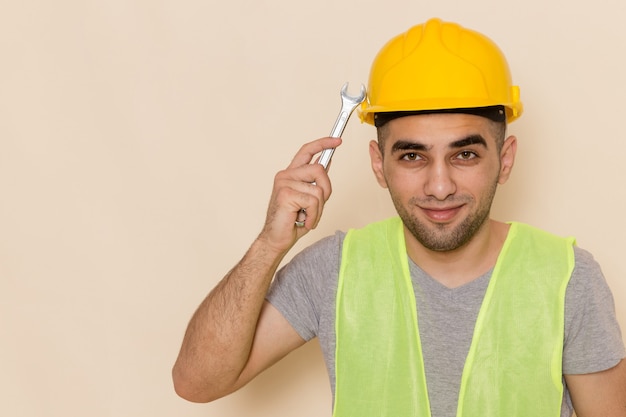 Constructor masculino de vista frontal en casco amarillo con herramienta plateada sobre el fondo claro