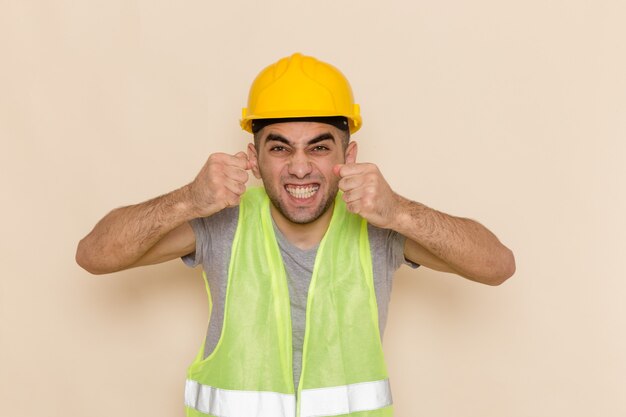 Constructor masculino de vista frontal en casco amarillo posando con expresión emocionada sobre el fondo claro