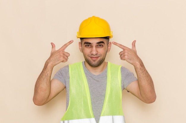 Constructor masculino de vista frontal en casco amarillo posando con expresión encantada sobre fondo claro