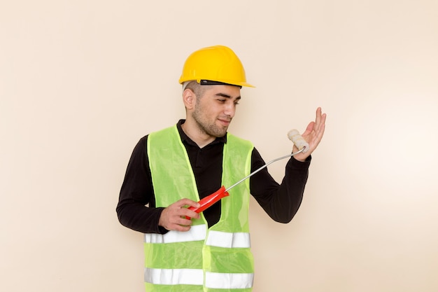 Foto gratuita constructor masculino de vista frontal en casco amarillo sosteniendo cepillo de pared sobre el fondo claro