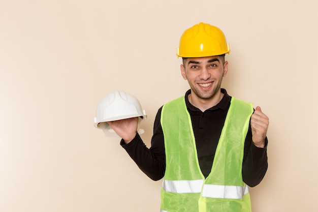 Foto gratuita constructor masculino de vista frontal en casco amarillo sosteniendo otro casco sobre fondo claro