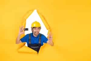 Foto gratuita constructor masculino de la vista frontal en uniforme que sostiene la tarjeta bancaria negra sobre fondo amarillo