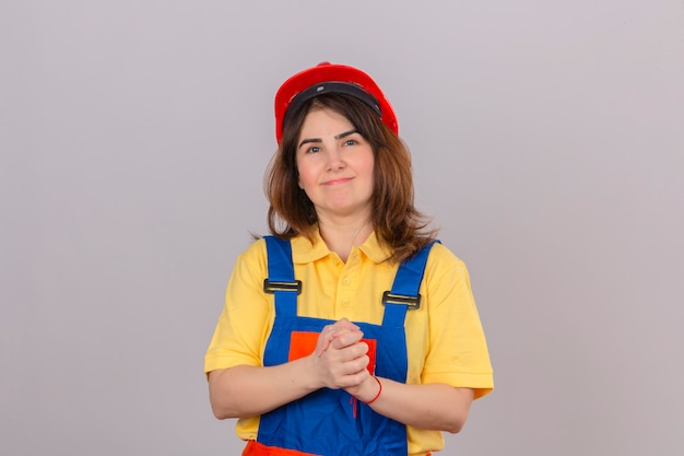 Constructor mujer vistiendo uniforme de construcción y casco de seguridad mirando confiado a la cámara sonriendo tomados de la mano juntos pensando en positivo sobre la pared blanca aislada