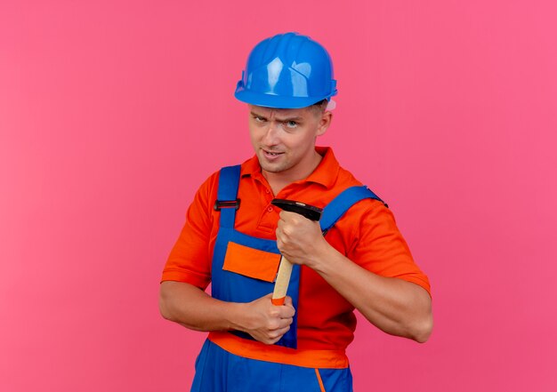 Constructor de sexo masculino joven confiado con uniforme y casco de seguridad con martillo