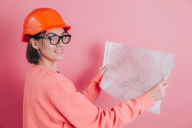 Constructor sonriente del trabajador de la mujer contra el fondo rosado. Casco de construcción.