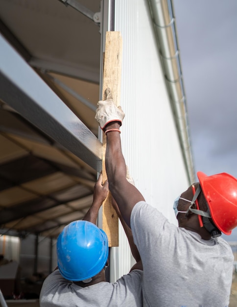 Constructores afroamericanos con cascos y mascarillas mientras miden el muro