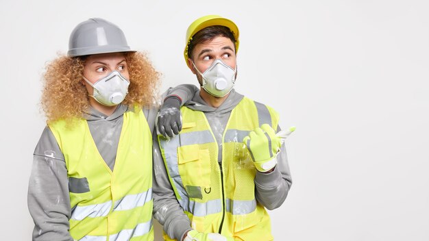 Constructores de hombres y mujeres con cascos de seguridad, respiradores y ropa de trabajo están juntos
