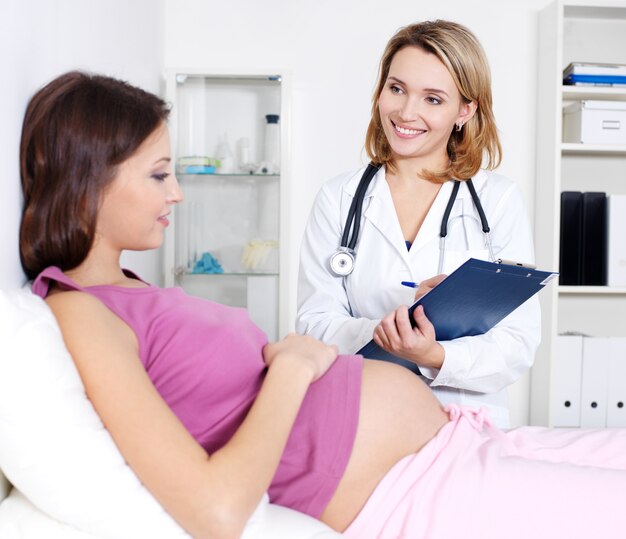 Consulta de la mujer joven embarazada con el médico en el hospital - en interiores