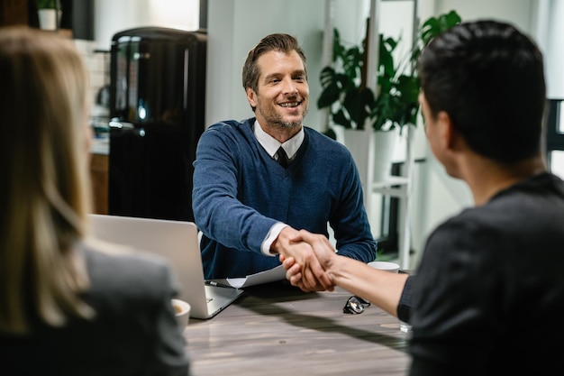 Un consultor financiero feliz saludando a sus clientes mientras se reunía con ellos en su casa Yo les estoy dando la mano