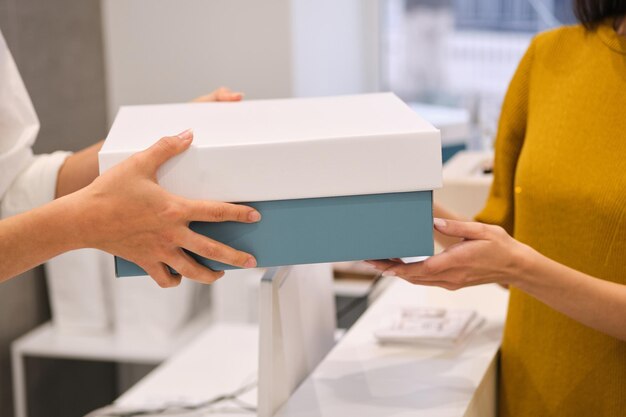 Consultor de moda de cerca dando ropa de embalaje al cliente en una tienda moderna