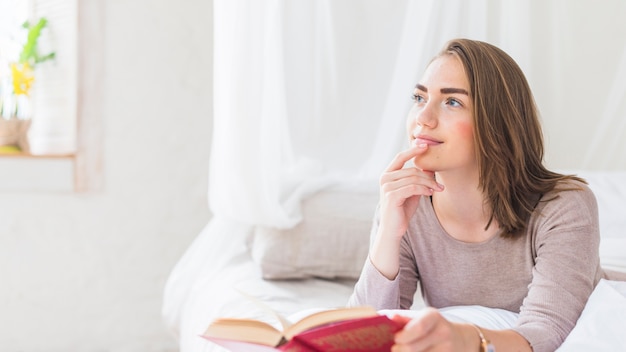 Contemplada hermosa joven mirando de lejos con el libro