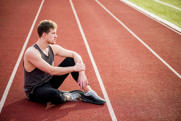 Contemplado joven atleta masculino sentado en la pista de carreras