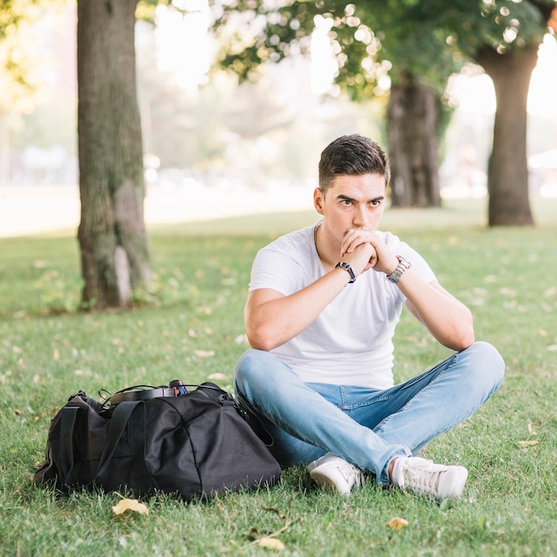 Foto gratuita contemplado joven sentado en la hierba