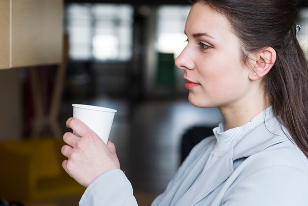 Contemplando atractiva empresaria sosteniendo la taza de café en la oficina