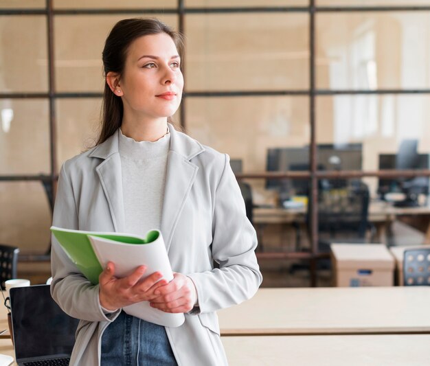 Contemplando hermosa empresaria sosteniendo el libro en el lugar de trabajo