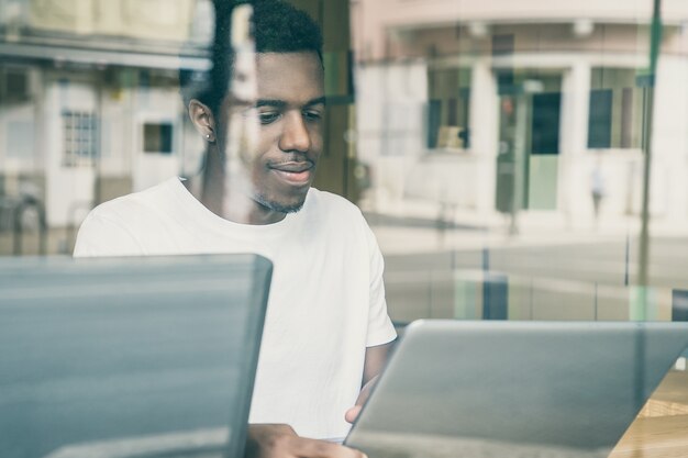 Contenido chico afroamericano sentado en la mesa y usando la computadora portátil