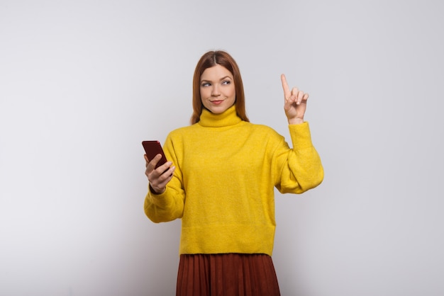 Contenido mujer sosteniendo teléfono inteligente y apuntando hacia arriba