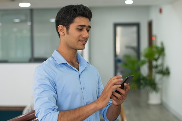 Contenido pensativo joven leyendo noticias de Internet en teléfono inteligente