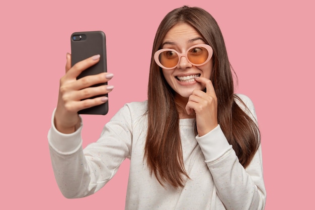 Contenido sonriente joven europea hace selfie a través de un teléfono inteligente para enviar en la aplicación de citas