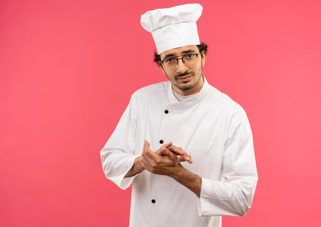 Contento joven cocinero vistiendo uniforme de chef y gafas cogidos de la mano juntos