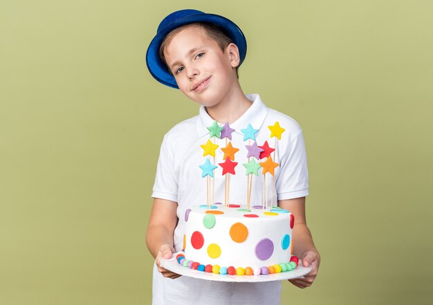 Contento joven muchacho eslavo con gorro de fiesta azul sosteniendo pastel de cumpleaños aislado en la pared verde oliva con espacio de copia