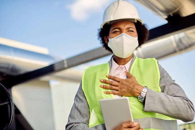 Contratista de obras negra con máscara facial que siente dolor en el pecho en el sitio de construcción