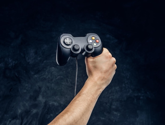 Controlador de consola de videojuegos en la mano del jugador contra el fondo de la pared oscura