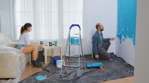 Conversación de pareja y renovación del hogar. Cepillo de rodillo bañado en pintura azul. Redecoración de apartamentos y construcción de viviendas mientras se renueva y mejora. Reparación y decoración.