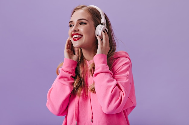 Cool girl en sudadera con capucha rosa escuchando música con auriculares blancos