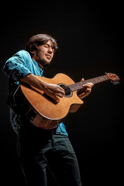 Cool guy parado con guitarra en la oscuridad