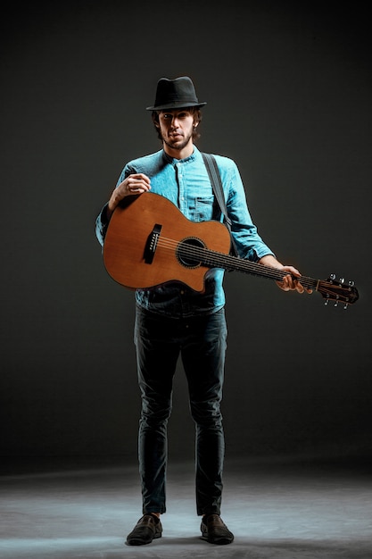 Cool guy parado con guitarra en la pared oscura