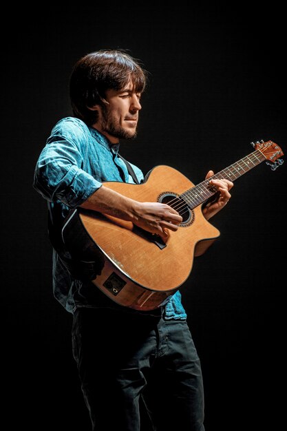 Foto gratuita cool guy parado con guitarra en la pared oscura