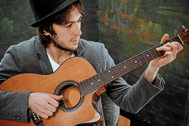 Cool guy con sombrero tocando la guitarra en el espacio gris