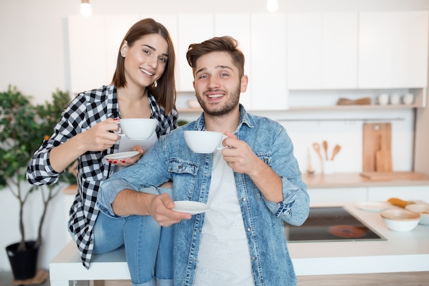 Cool hipster joven feliz y mujer en la cocina, desayuno, pareja juntos en la mañana, sonriendo, tomando té