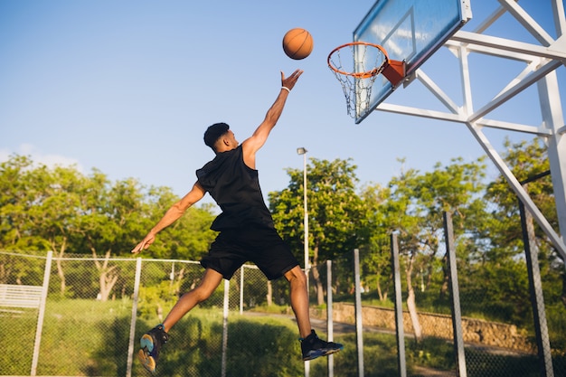 Cool hombre negro haciendo deportes, jugando baloncesto al amanecer, saltando