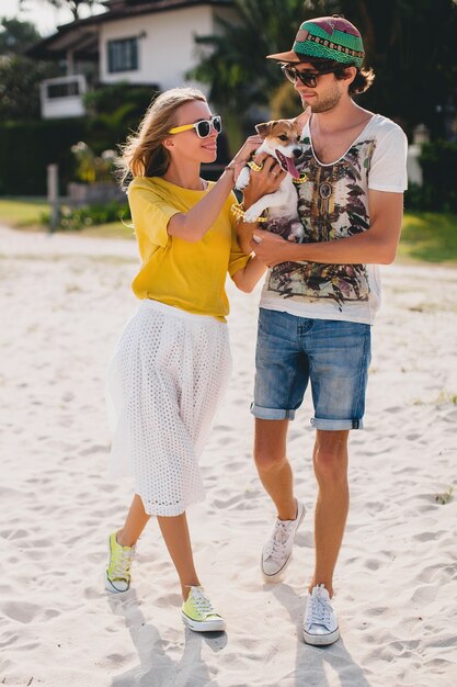 Cool joven hipster elegante pareja enamorada caminando jugando perro cachorro jack russell en playa tropical, arena blanca, estado de ánimo romántico, divirtiéndose, soleado, hombre mujer juntos, vacaciones