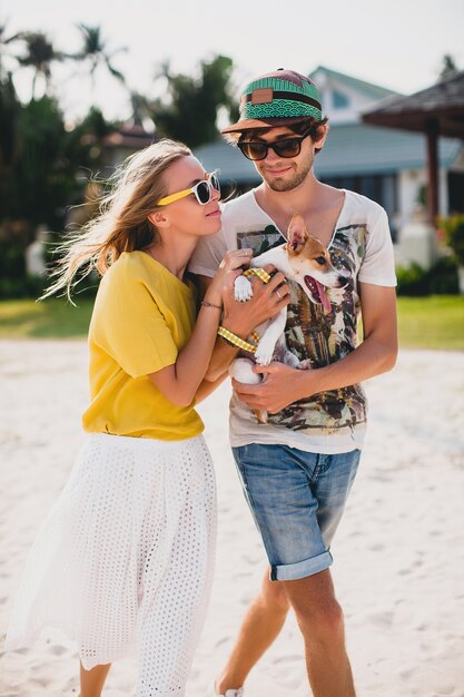 Cool joven hipster elegante pareja enamorada caminando jugando perro cachorro jack russell en playa tropical, arena blanca, estado de ánimo romántico, divirtiéndose, soleado, hombre mujer juntos, vacaciones