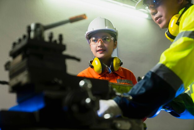 Cooperación de ingenieros Dos ingenieros de mantenimiento asiáticos, hombres y mujeres, inspeccionan el sistema de protección de relés con un dispositivo de tableta para controlar el proceso de control de calidad en una fábrica de fabricación de la industria pesada