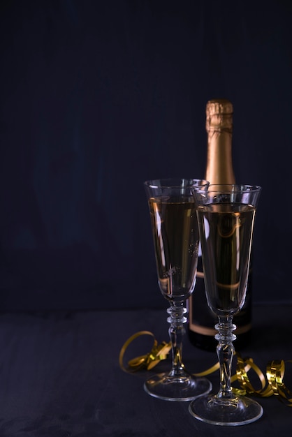 Foto gratuita copa de champán y botella con serpentinas sobre fondo negro