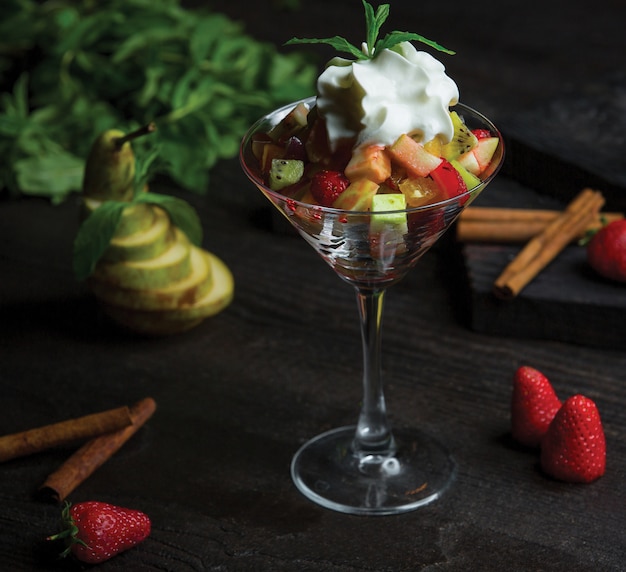 Una copa de cóctel llena de ensalada de frutas y crema batida