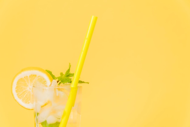 Copa de coctel con paja y limón sobre fondo amarillo