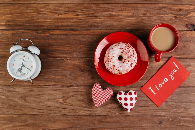 Copa y donut en plato entre las decoraciones de san valentín.