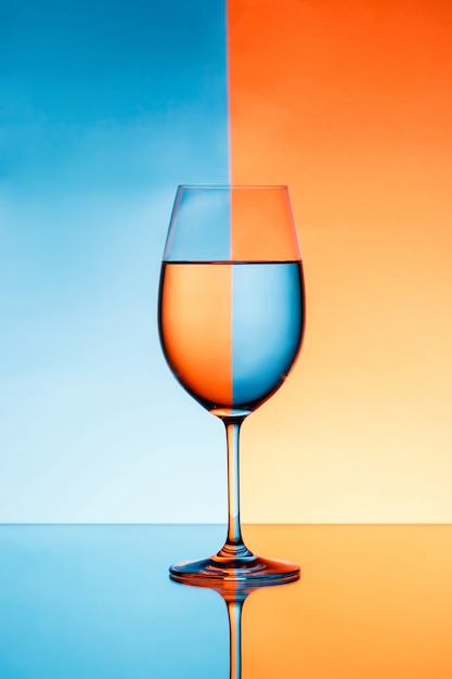 Copa de vino con agua sobre fondo azul y naranja.