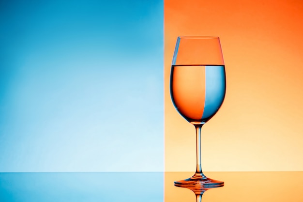 Copa de vino con agua sobre fondo azul y naranja.