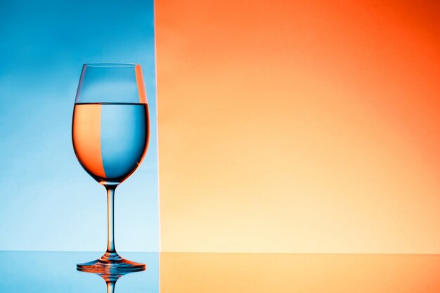 Copa de vino con agua sobre fondo azul y naranja.