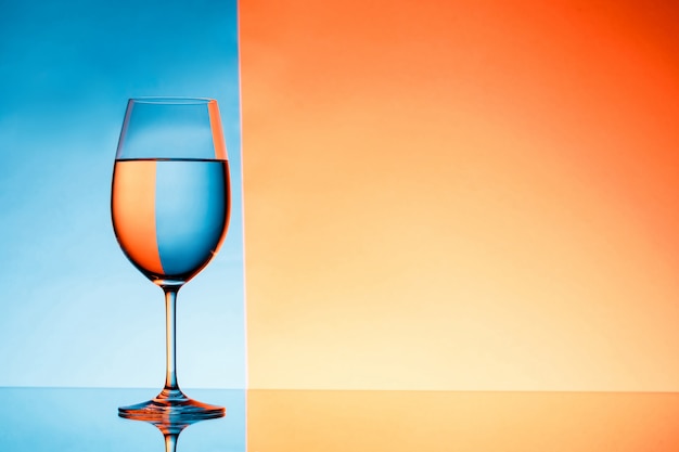 Copa de vino con agua sobre fondo azul y naranja.