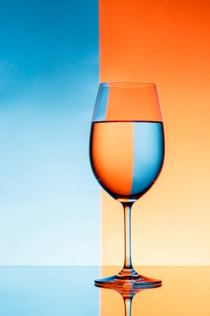 Copa de vino con agua sobre pared azul y naranja