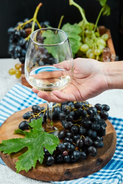 Una copa de vino blanco con un racimo de uvas rojas alrededor.